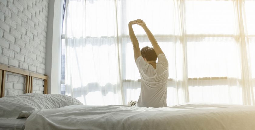 Man sitting at edge of bed and stretching his arms in the morning